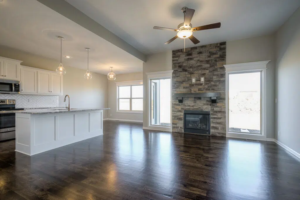 Open-concept Living Area With Hardwood Floors, Stone Fireplace, And Adjoining Kitchen By Comerio Homes