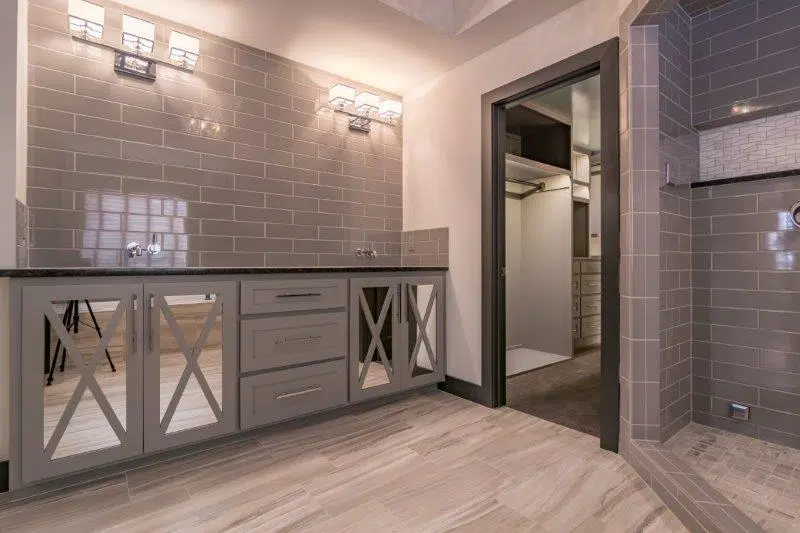 Justina Bathroom Featuring A Custom Vanity With Mirrored Cabinet Doors, Gray Tile, And An Adjoining Walk-in Shower.