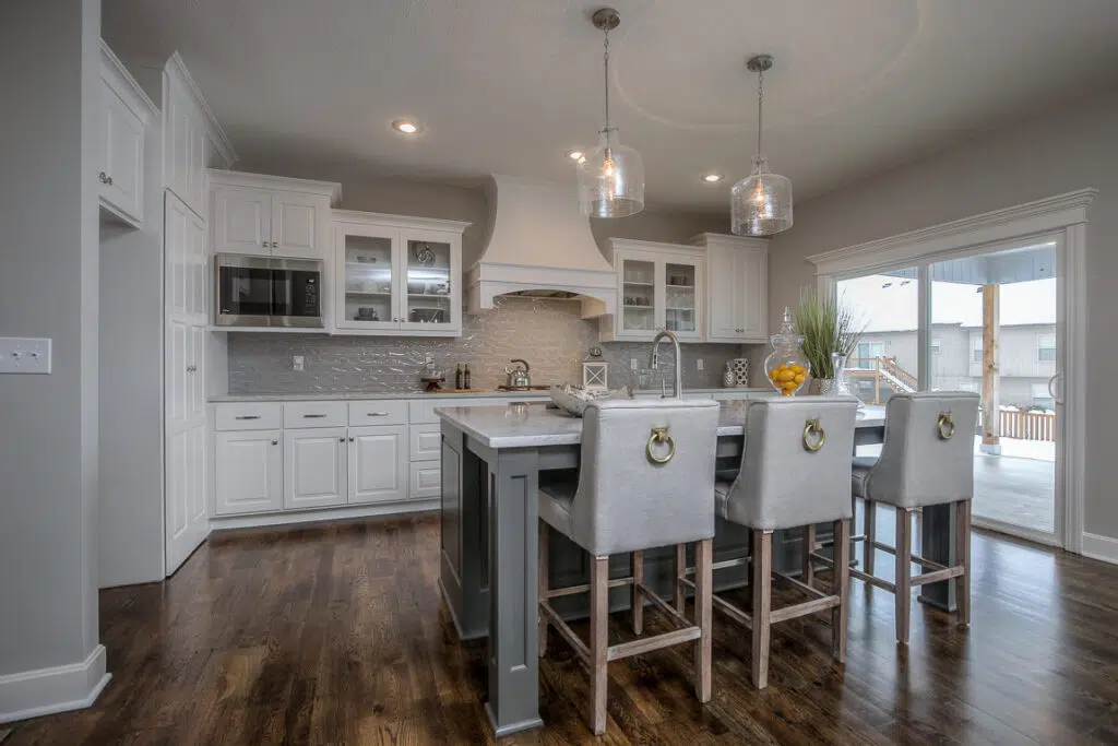 Custom Kitchen With White Cabinetry, Large Island, Herringbone Backsplash, And Hardwood Floors By Comerio Homes