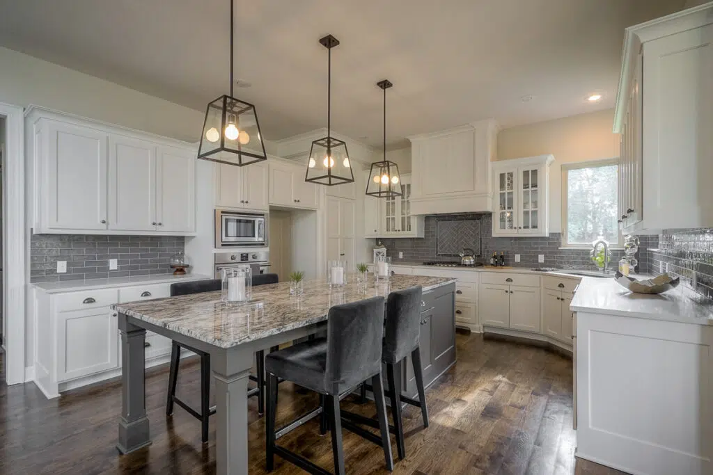 Custom Kitchen With White Cabinetry, Large Island, Granite Countertops, And Pendant Lighting By Comerio Homes
