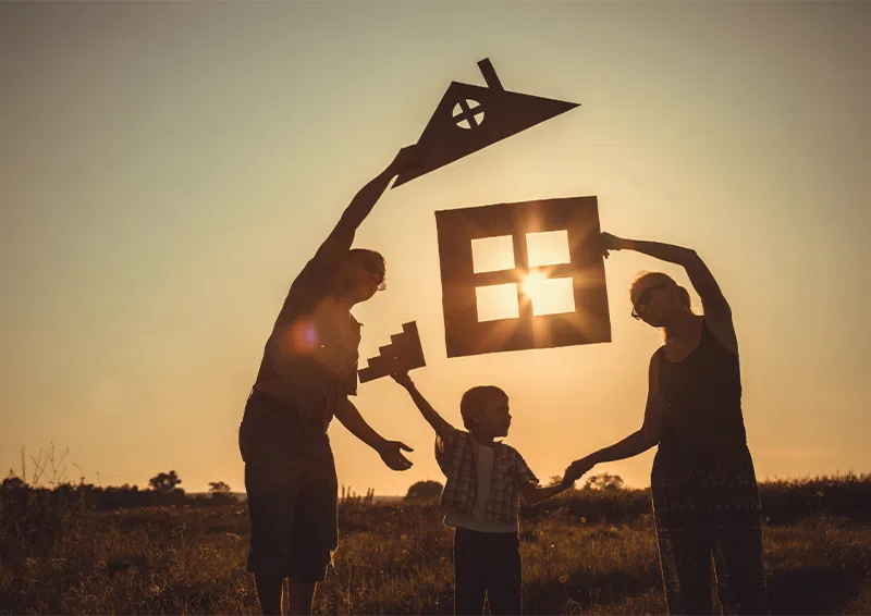 Family Holding House-shaped Cutouts Together At Sunset
