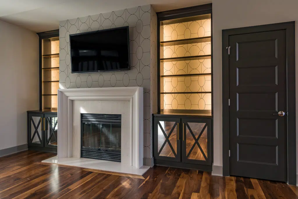 Justina Floor Plan Living Room By Comerio Homes Featuring A Fireplace, Illuminated Built-in Shelving And Custom Cabinetry.