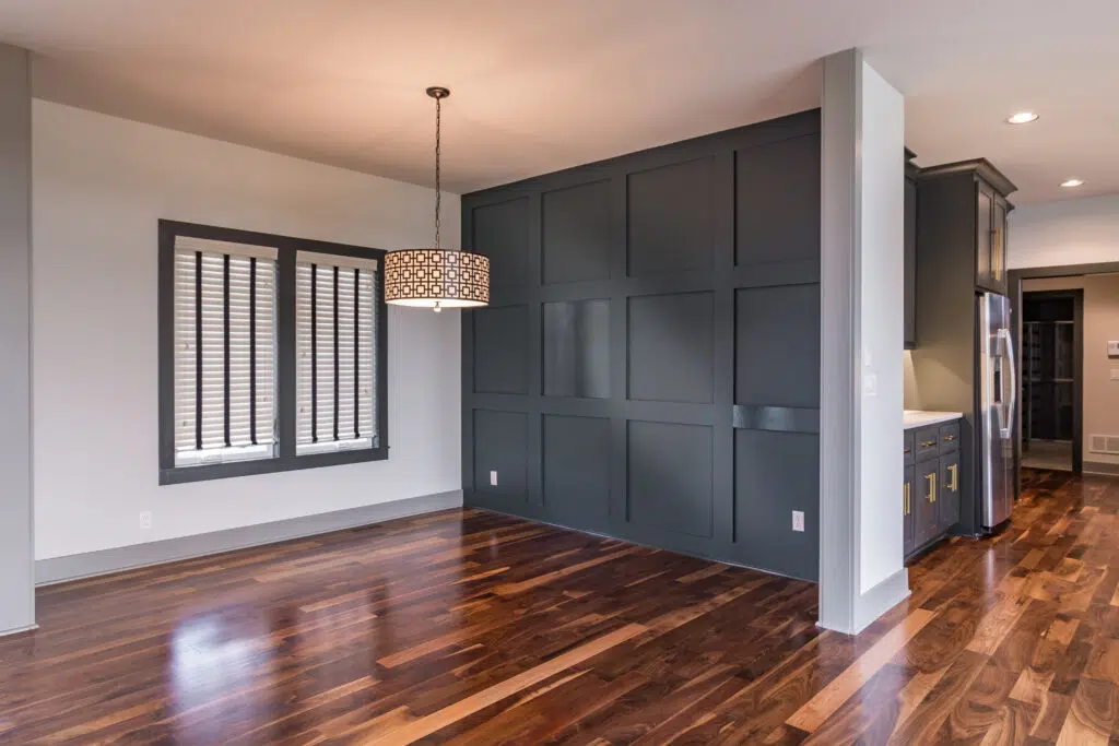 Justina Floor Plan Dining Room By Comerio Homes With Dark Paneled Accent Wall, Hardwood Flooring And Statement Lighting.