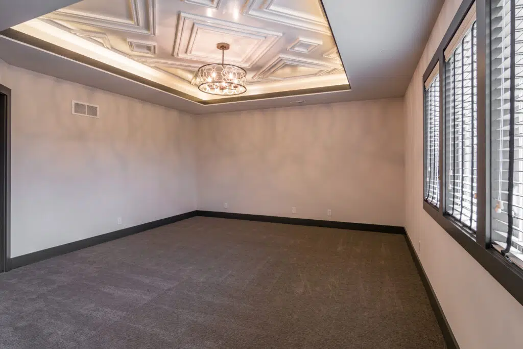 Justina Floor Plan Bedroom By Comerio Homes With Carpeted Flooring, Large Windows And An Illuminated Coffered Ceiling.