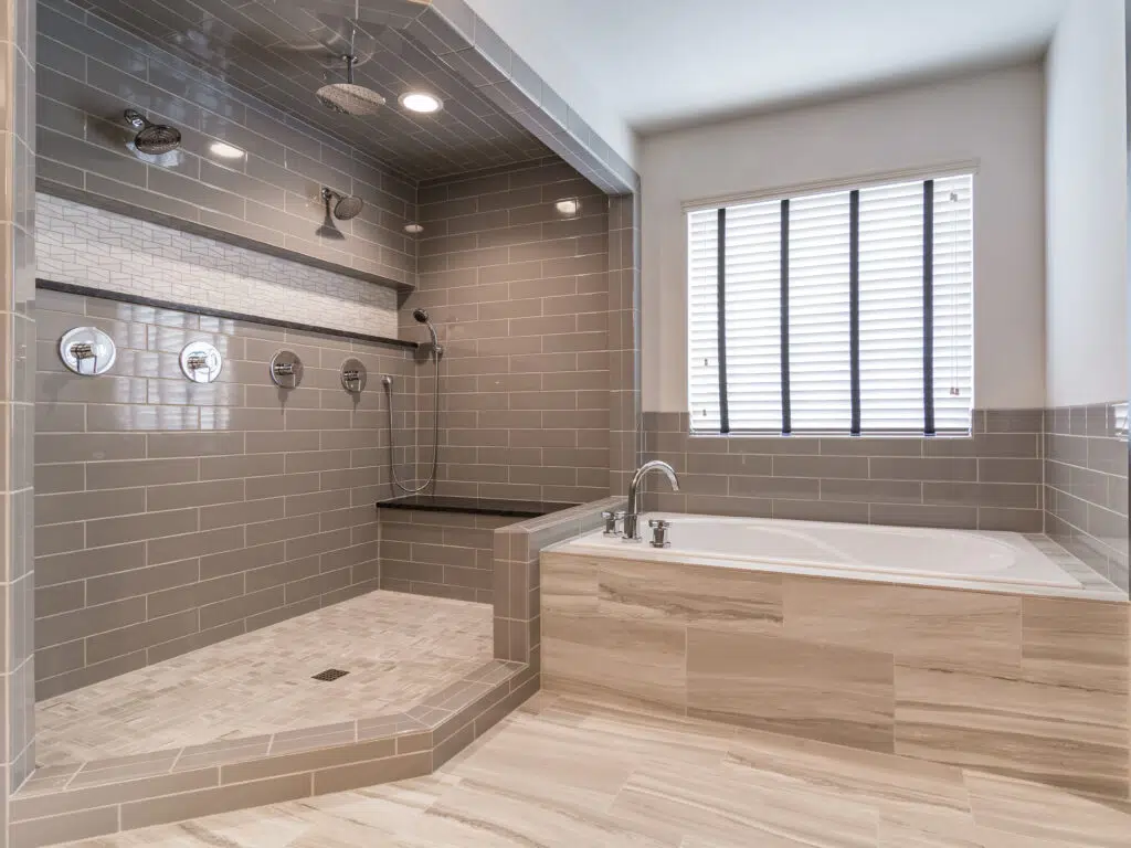 Justina Floor Plan Primary Bathroom By Comerio Homes Featuring A Large Tiled Walk-in Shower With Multiple Showerheads And Soaking Tub.
