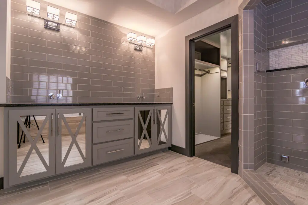 Justina Floor Plan Primary Bathroom By Comerio Homes With Custom Vanity Cabinetry, Gray Tile Walls And Walk-in Shower.