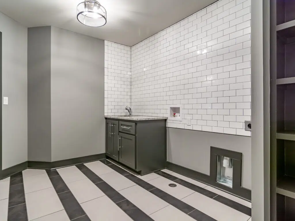 Justina Floor Plan Laundry Room By Comerio Homes Featuring Cabinetry, Utility Sink, Subway Tile Walls And Patterned Tile Flooring.