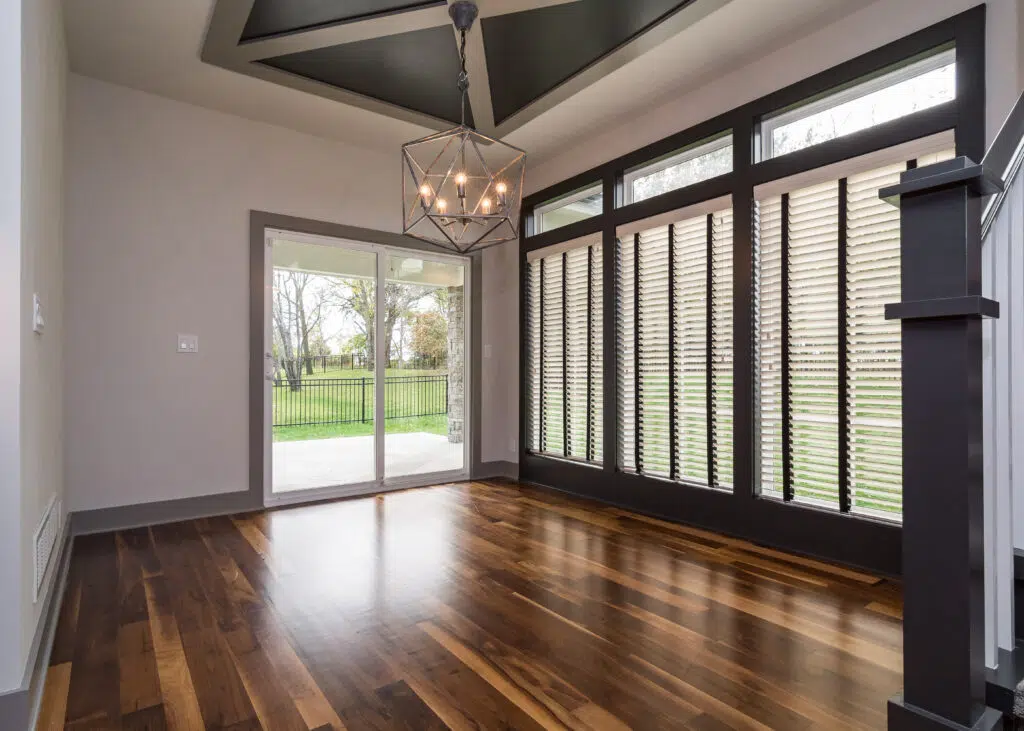 Justina Floor Plan Dining Area By Comerio Homes Featuring Hardwood Floors, Large Windows, Geometric Ceiling Detail And Pendant Lighting.