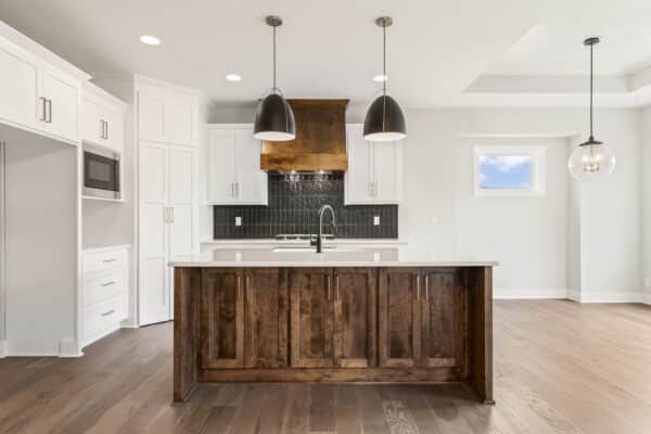 The interior of a modern home's kitchen, featuring ample space, island with contrasting, dark-finish fixtures, and dark subway tile. The Siena home plan as designed by Comerio Homes.
