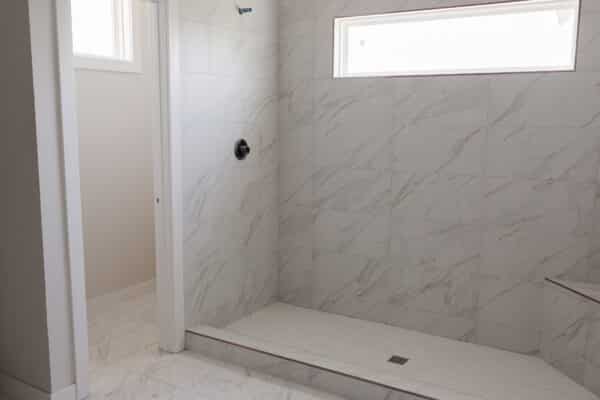A modern home's bathroom interior, featuring marble shower area with integrated seating. Part of the Siena home plan as designed by Comerio Homes.