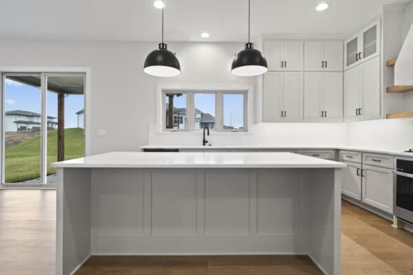 A modern, well-lit kitchen with sweeping views of the outdoor landscaping. The kitchen features dark-finish fixtures, featured within the Milano home plan, designed by Comerio Homes. Located in Coventry Valley, Overland Park.