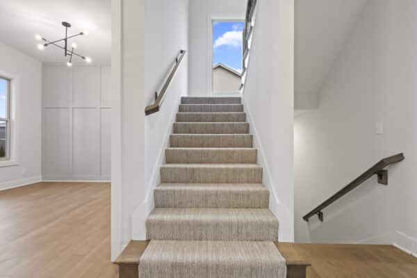The Milano home design's main stairwell from the main level. The main level living area is flooded with natural light and wood flooring. Designed by Comerio Homes.