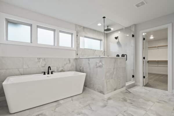 The Milano home design's master bath suite, featuring modern finishes and free standing bath tub next to a custom shower room with ample natural lighting.