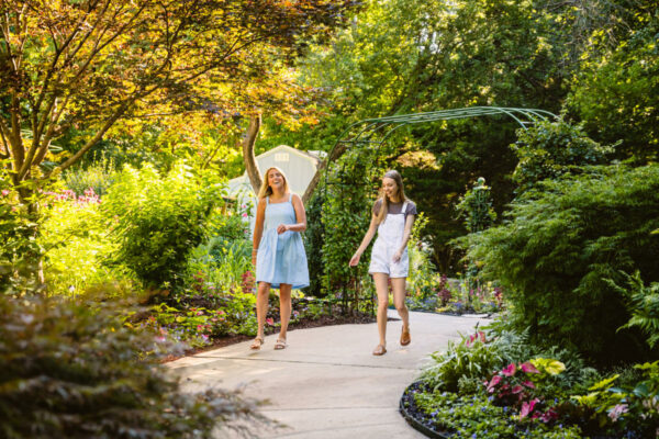 A pair of people in light Spring clothing walking along a paved path in the Overland Park Arboretum and Botanical Gardens.