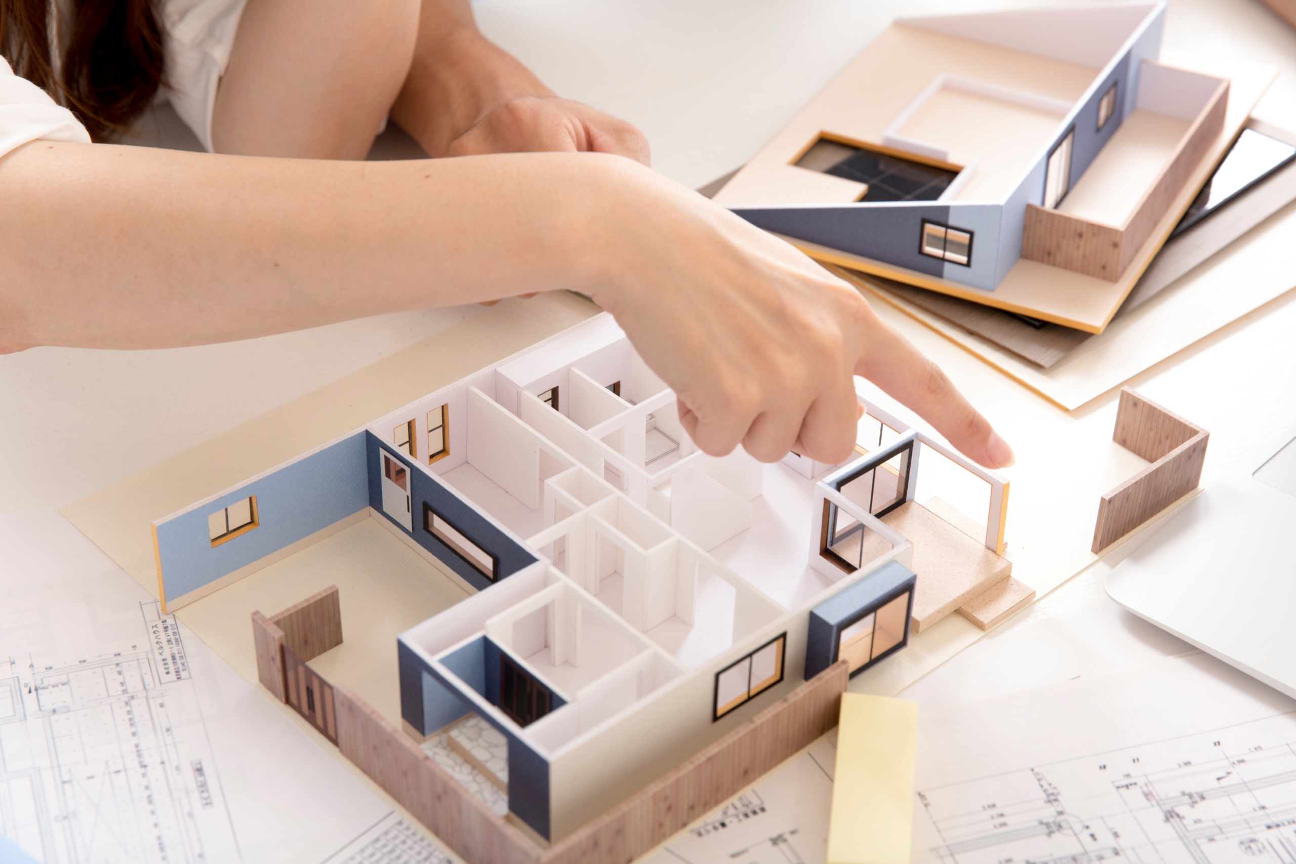 A person pointing over a combination of 2D and 3D paper cut-out floor plan design elements at a table.