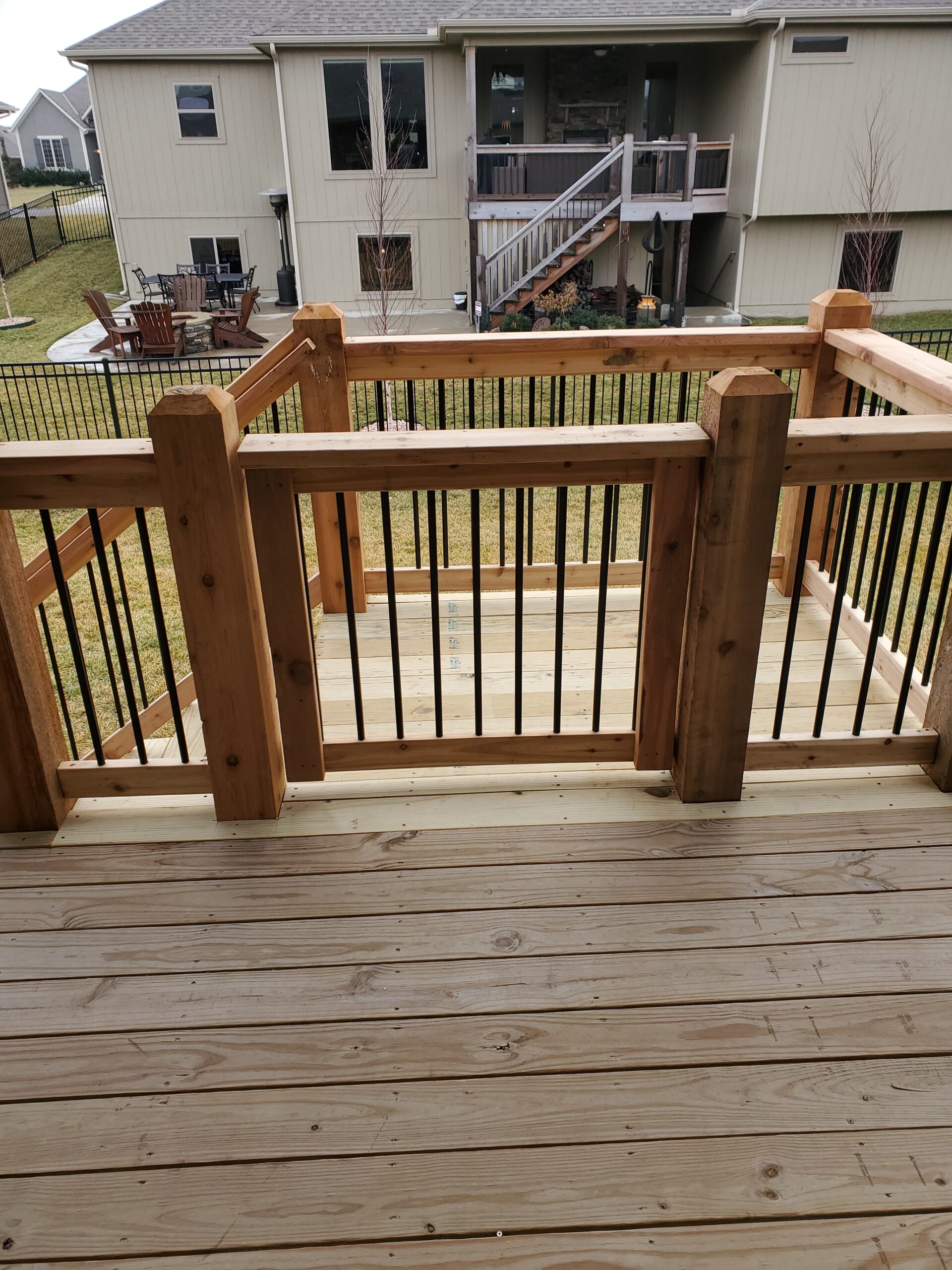 Wood Deck With Stairs And Black Metal Balusters Creating An Outdoor Living Space Overlooking A Residential Backyard.