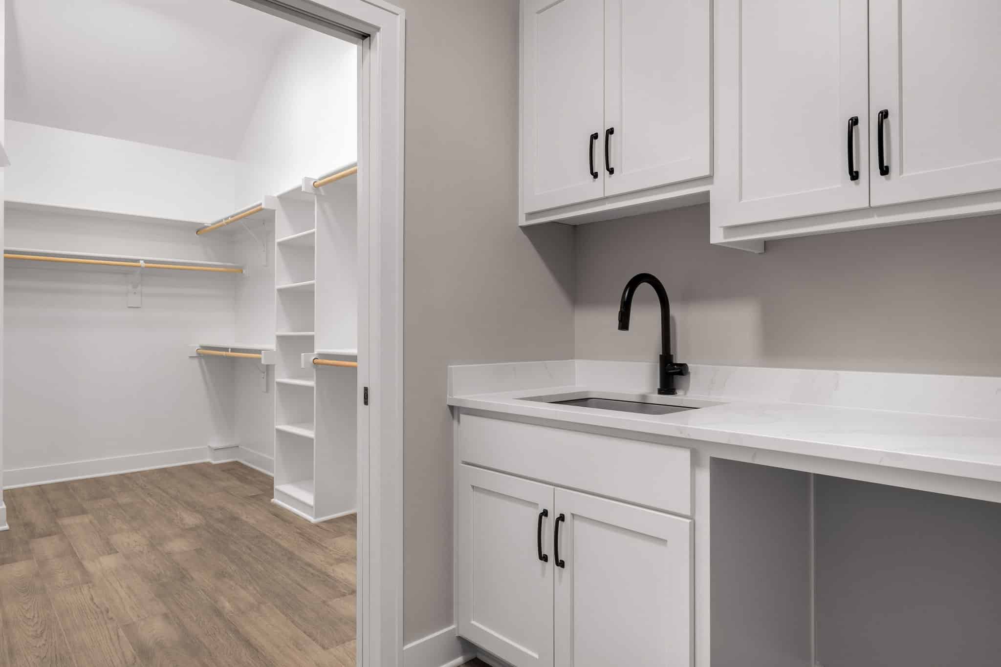 Madalena Laundry Room Sink With White Shaker Cabinets, Quartz Countertop, Brass Hardware, Open Shelving, And Hanging Rod.