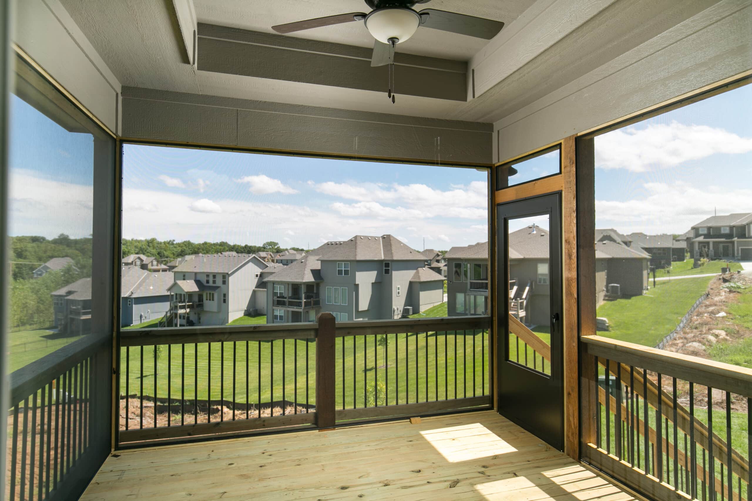 Madalena Screened-in Porch With Wood Railings, Black Balusters, Screen Door, And Views Of The Wooded Backyard.