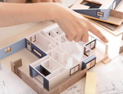 Hands Working On A Home Floor Plan Model Representing Custom Home Design And Planning