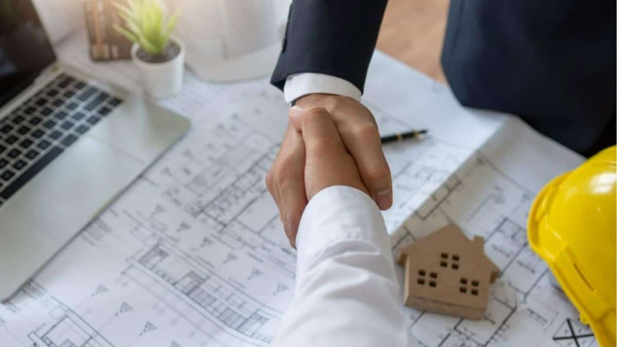 Handshake over home blueprints representing agreement and partnership in home building process by Comerio Homes