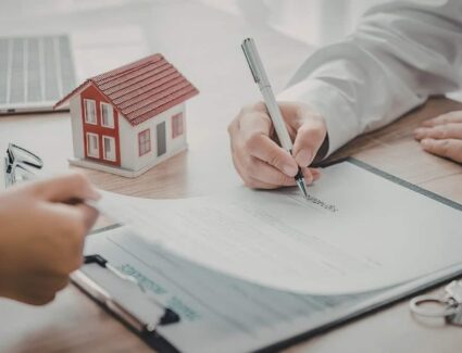 Homeowner Signing Home Building Contract And Agreement Documents With Model House By Comerio Homes