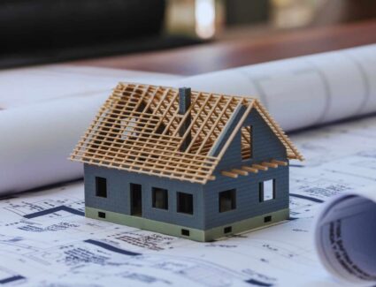 Model House Under Construction On Architectural Blueprints Representing Home Design And Building Process