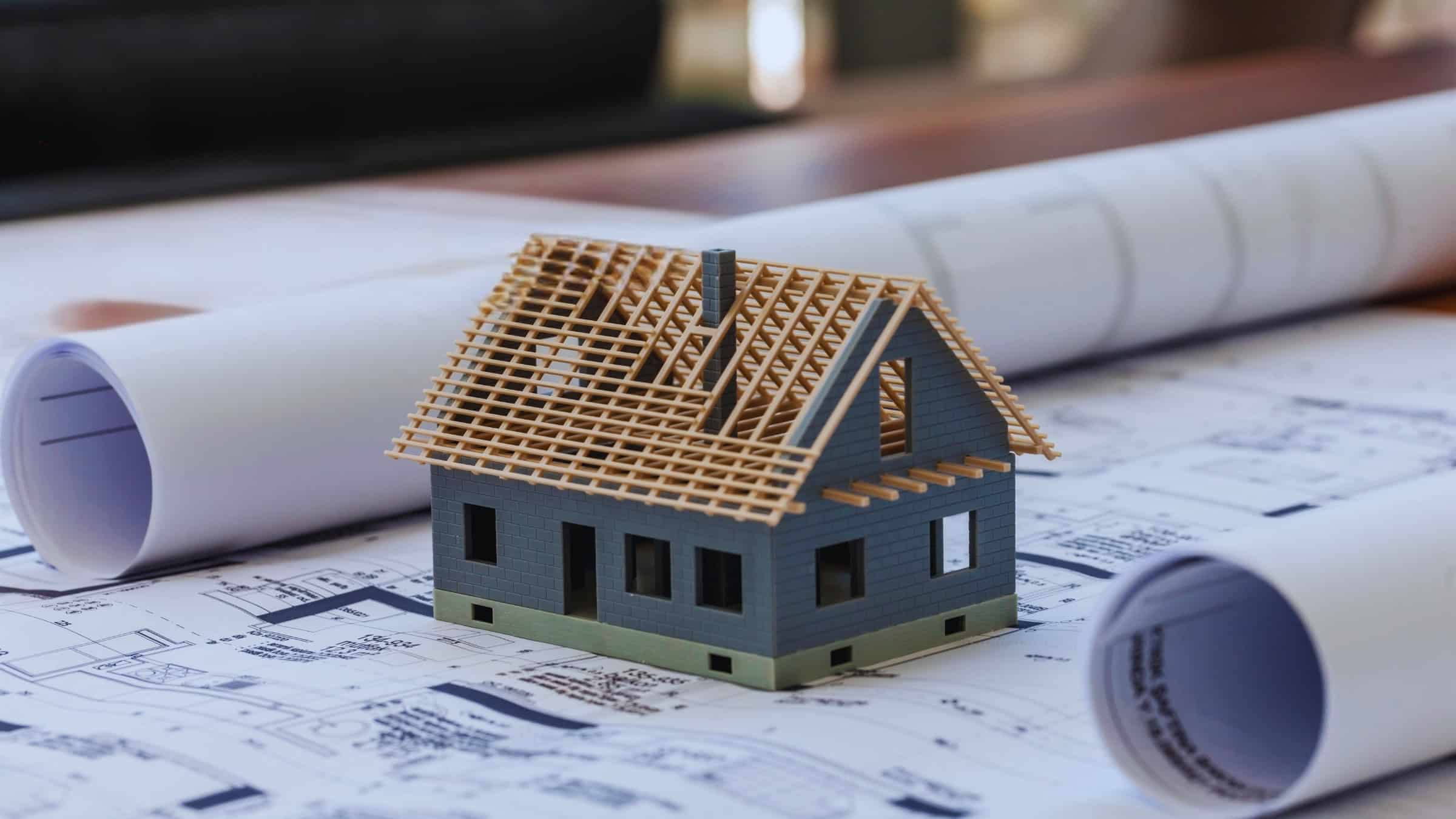Model House Under Construction On Architectural Blueprints Representing Home Design And Building Process